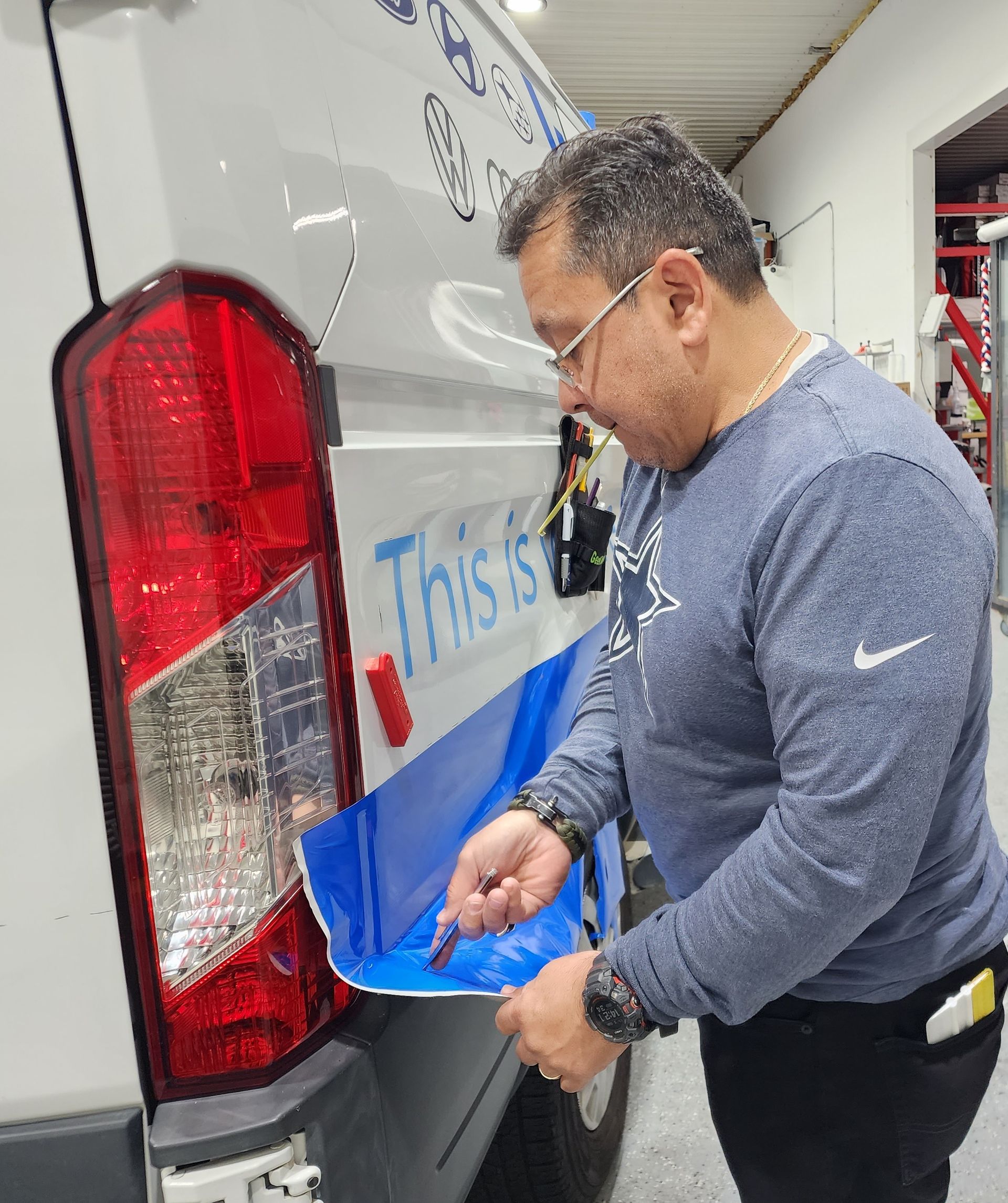 A man is wrapping a van with blue tape that says this is