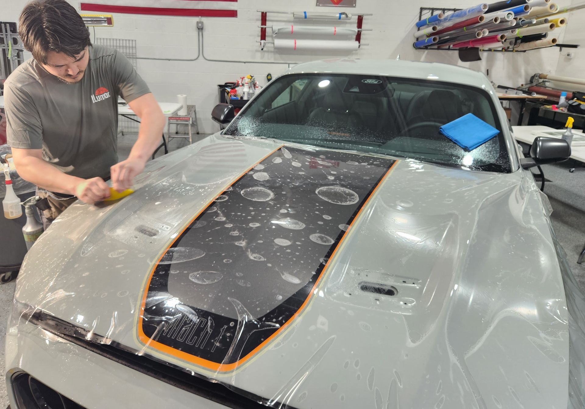 A man is covering the hood of a white car with plastic wrap.
