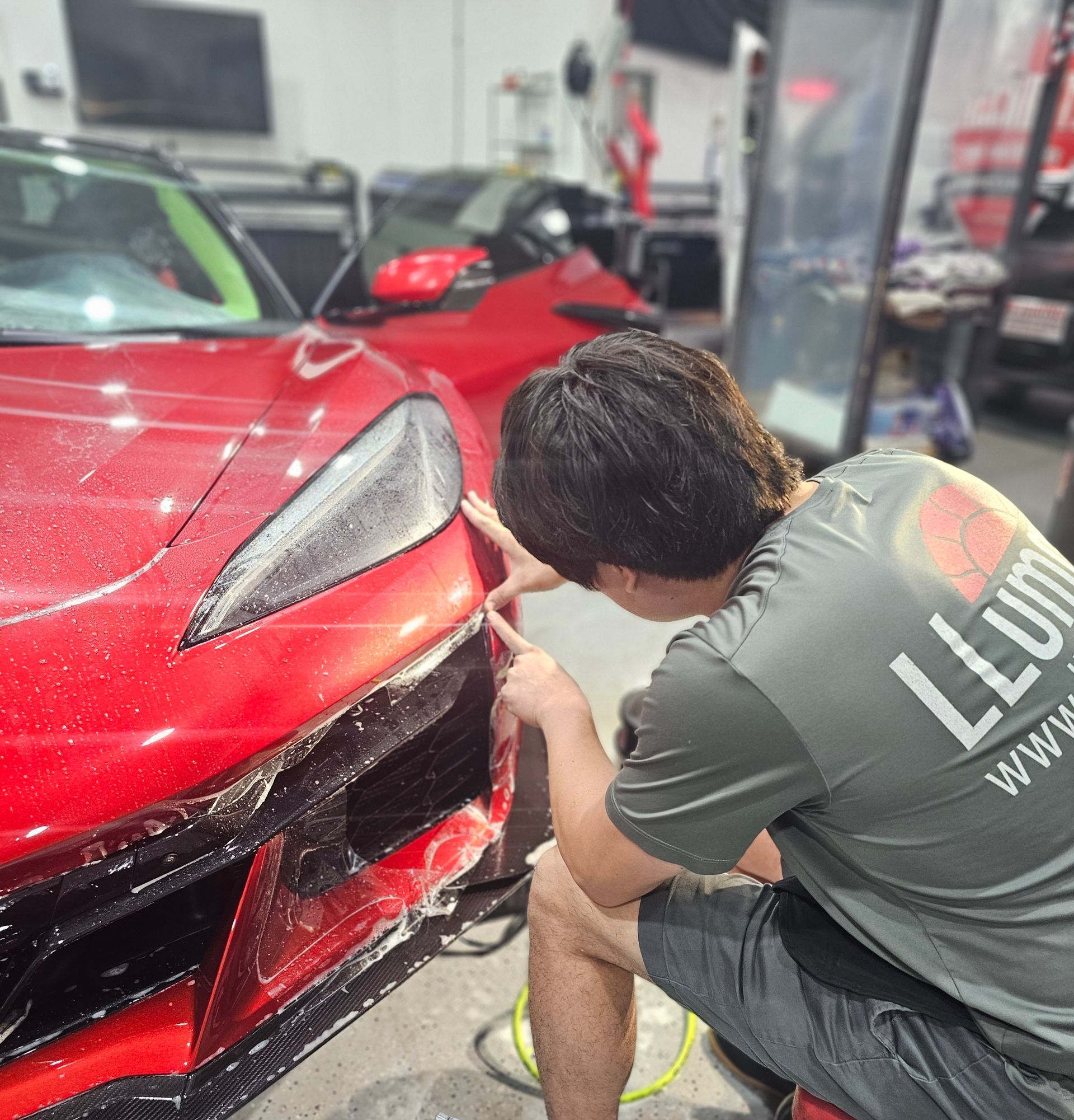A man is kneeling down in front of a red sports car.