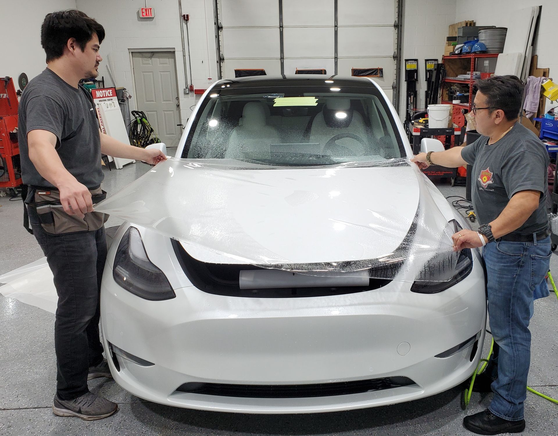 Two men are wrapping a white tesla model y in plastic.