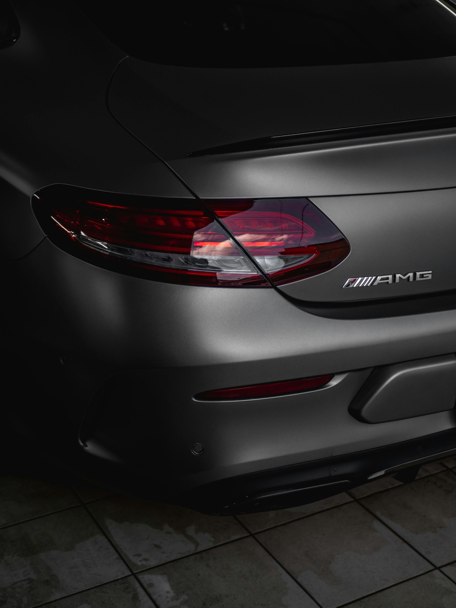 A close up of the back of a silver car parked on a tiled floor.