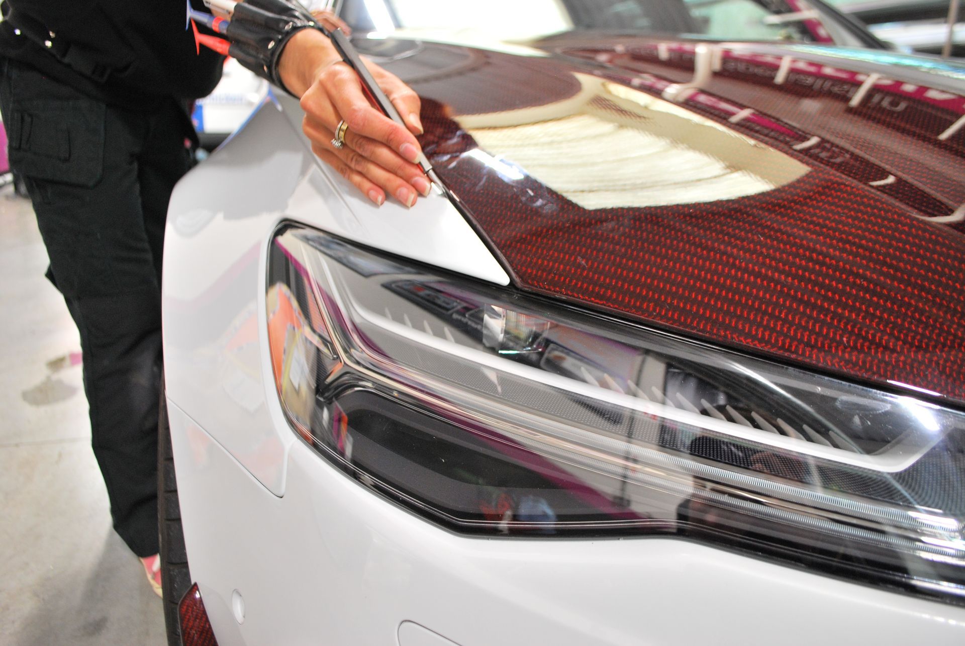 A woman is writing on the hood of a white car.