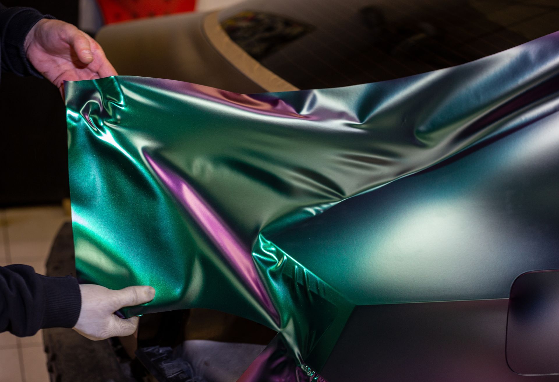A man is kneeling down in front of a red sports car.