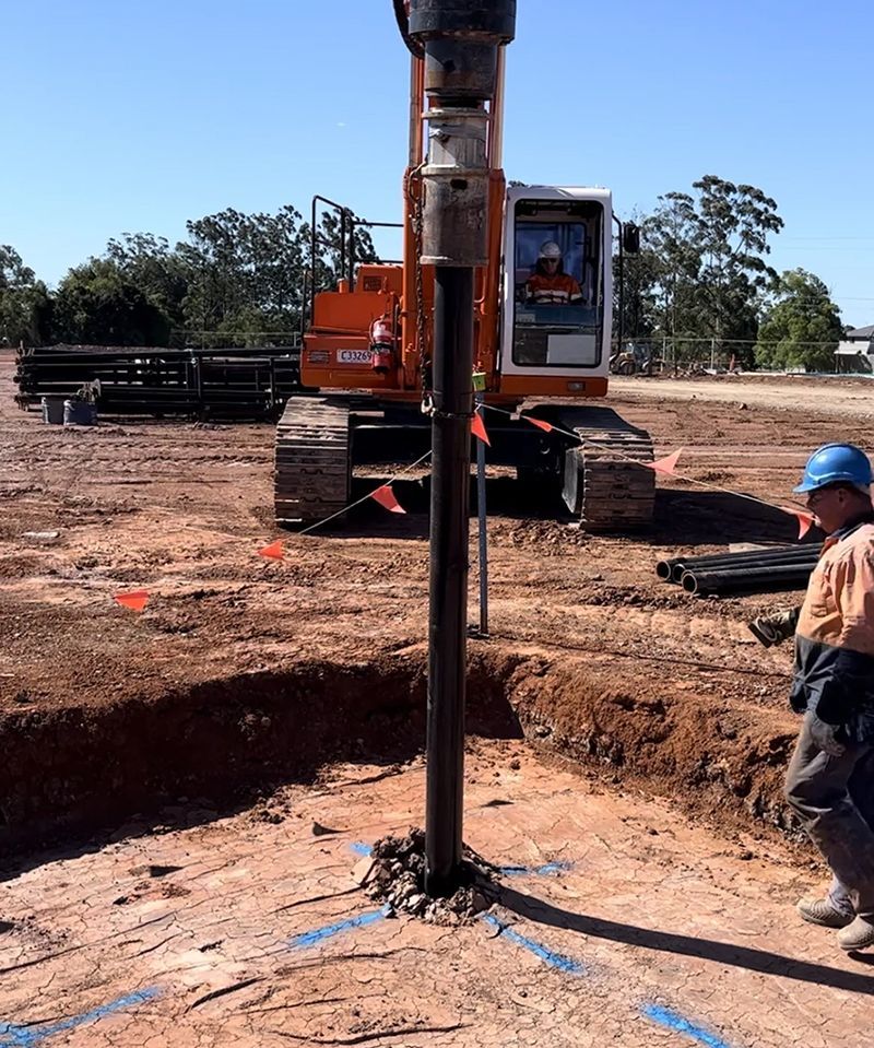 A Man in a Hard Hat Stands in Front of a Large Orange Excavator — Hardarc Engineering in Coolum Beach, QLD