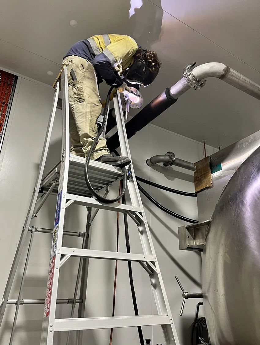 A Man is Standing on a Ladder Welding a Pipe — Hardarc Engineering in Coolum Beach, QLD