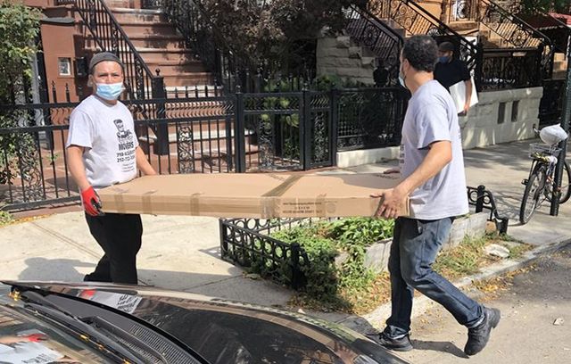 two men wearing masks are carrying a large cardboard box