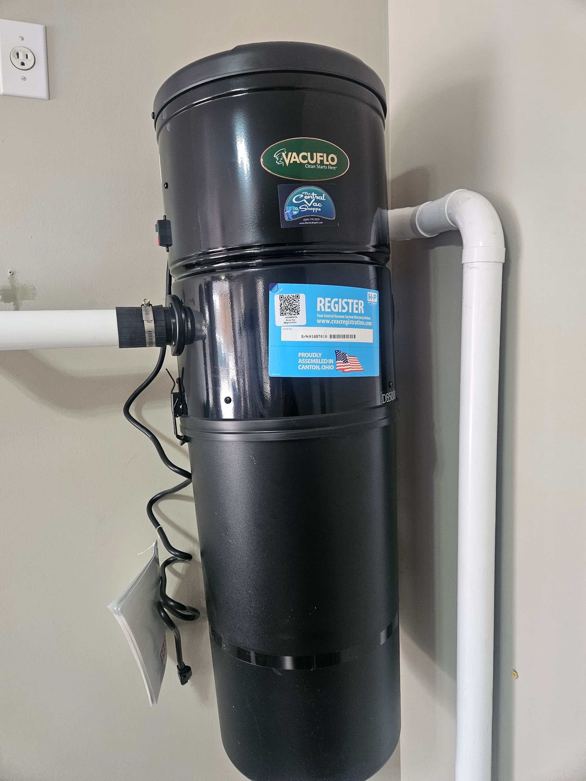 A black vacuum cleaner is attached to a white pipe on a wall.