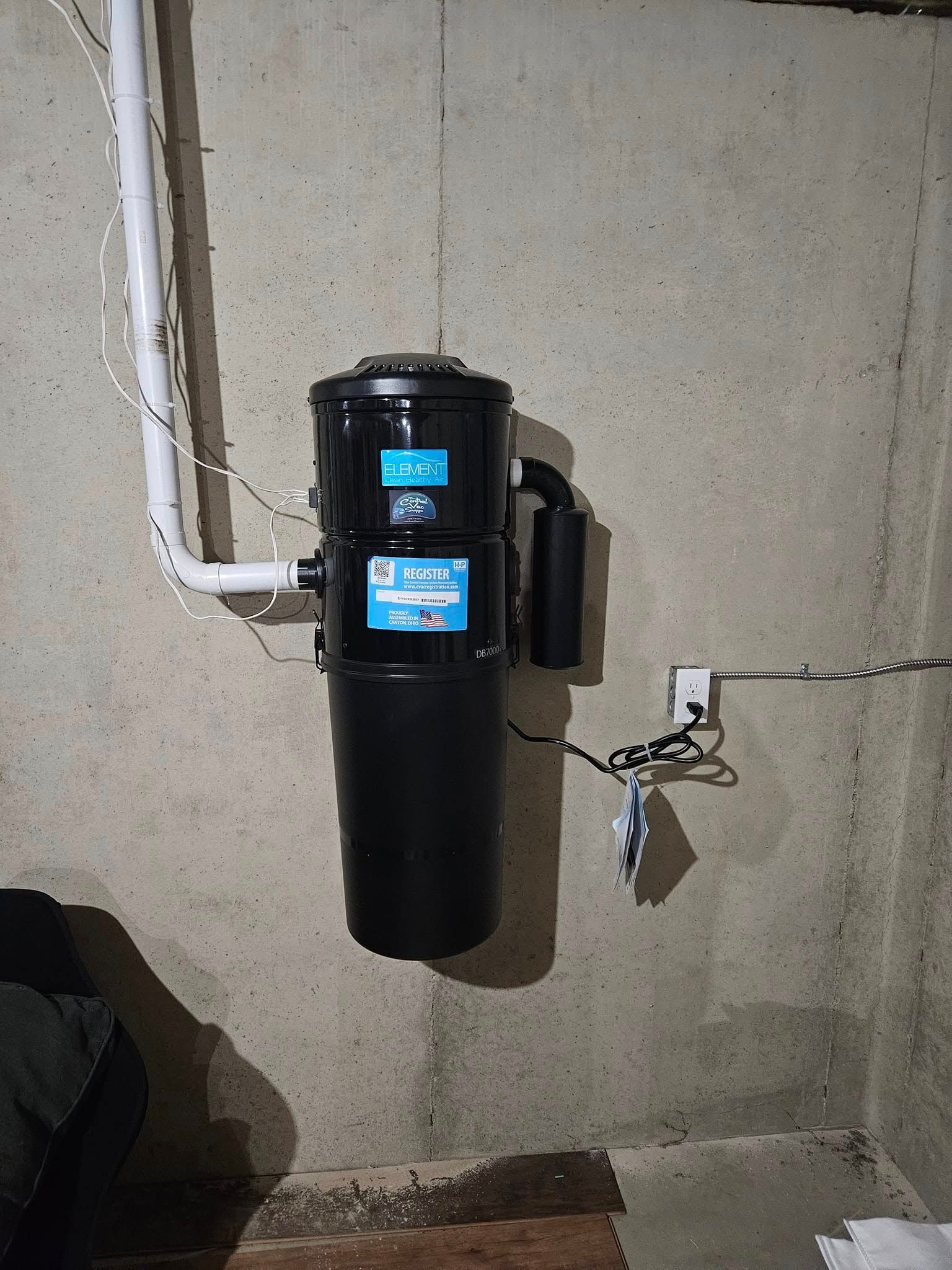 A black vacuum cleaner is hanging on a wall in a basement.