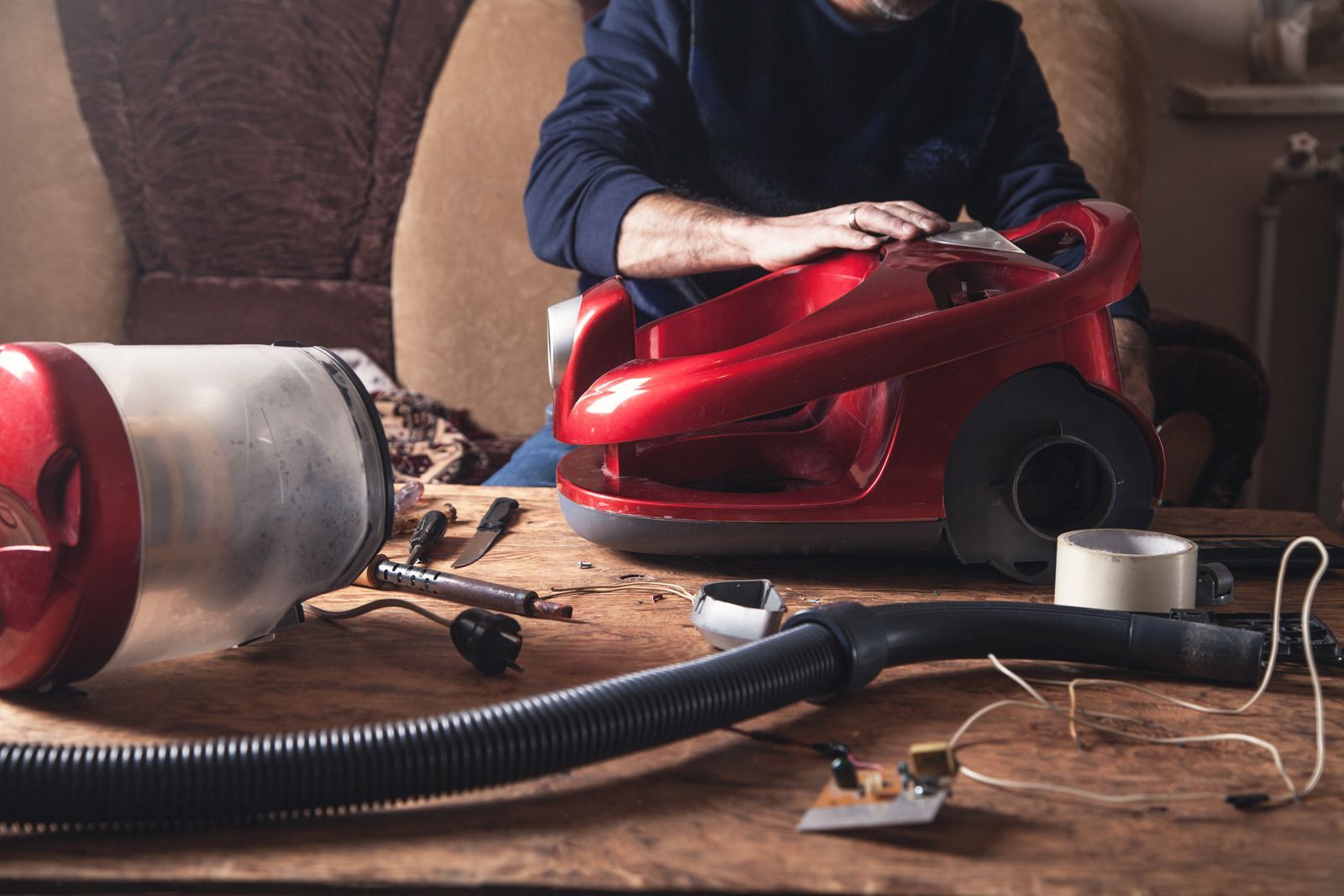 A man is sitting at a table repairing a vacuum cleaner.