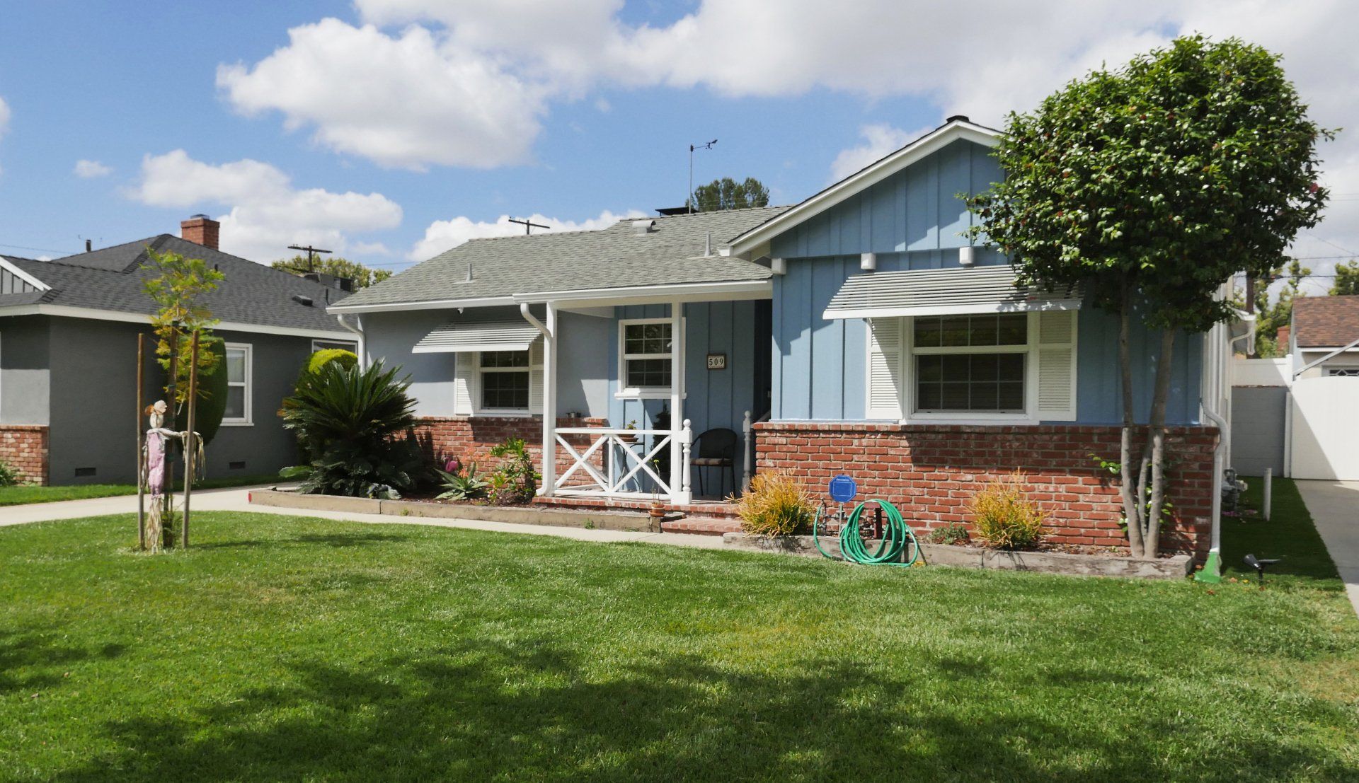 Blue and brick house with green lawn under a partly cloudy sky.