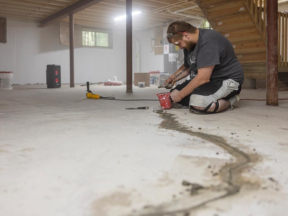 A man works on a concrete floor in a basement for Crackstoppers Foundation Repair & Waterproofing in