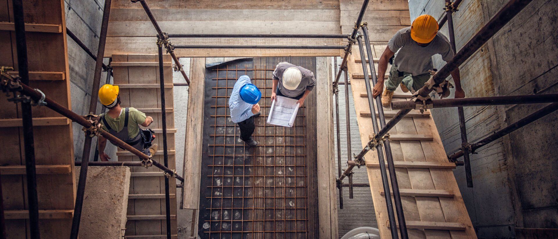 Construction workers in hard hats on a scaffolding, reviewing blueprints.