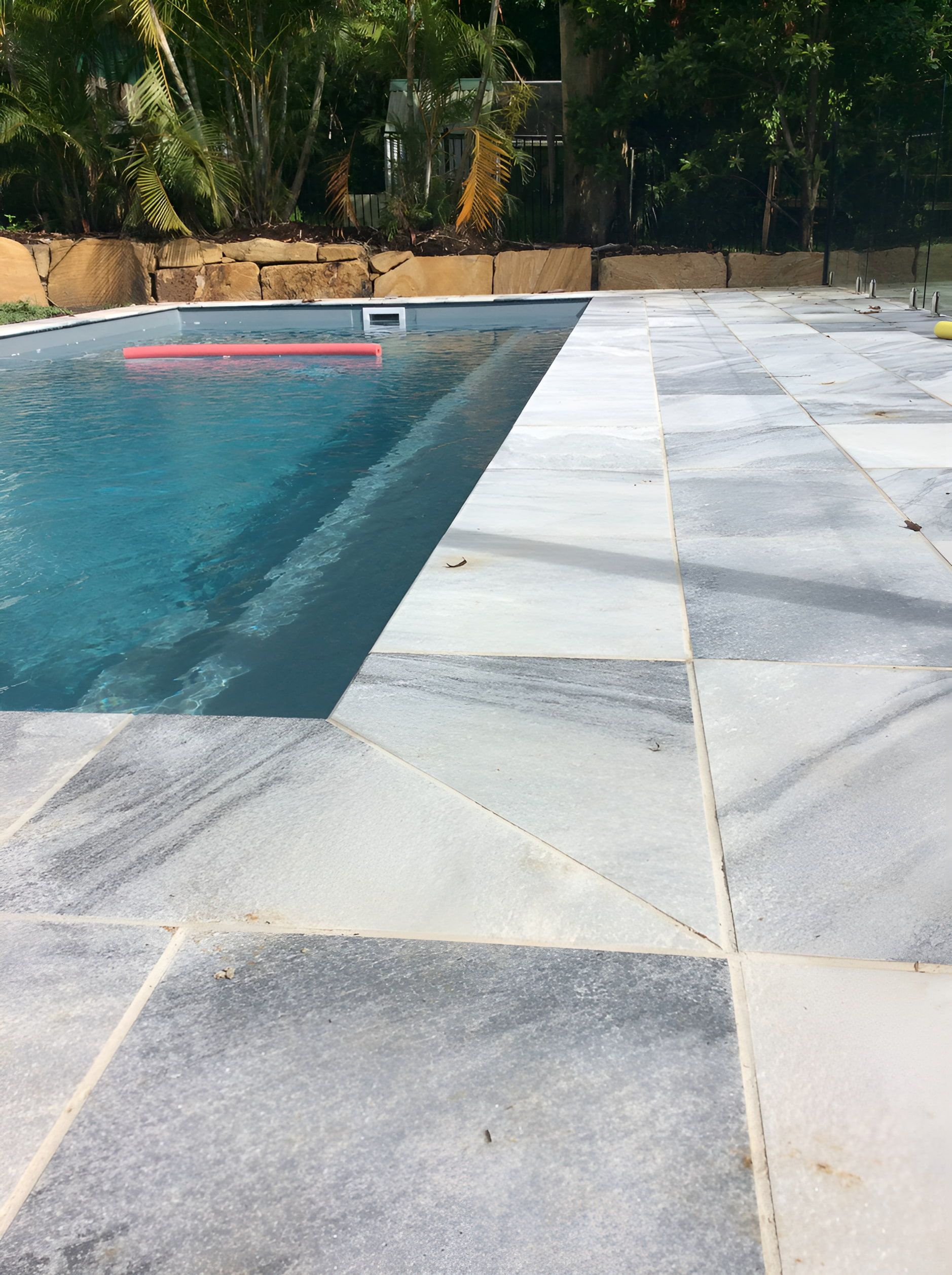 A Swimming Pool Is Surrounded By A Tiled Patio And Trees — Mid Coast Tiles Urunga In Urunga, NSW