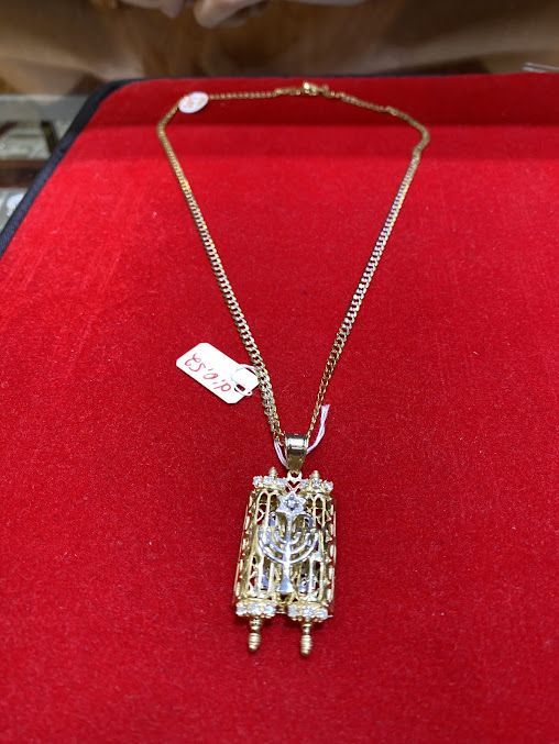 A gold necklace with a torah pendant on it