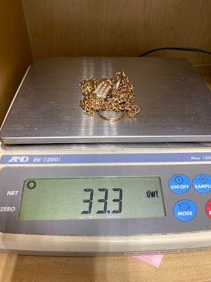 A necklace and ring are being weighed on a scale.