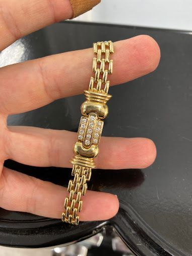 A person is holding a gold bracelet in their hand