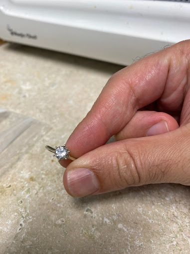 A person is holding a diamond ring on their finger.