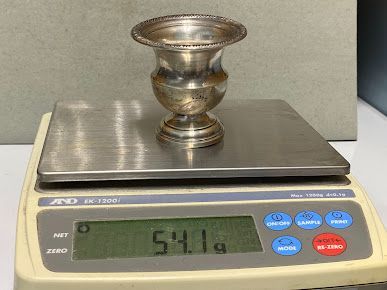 A silver vase is sitting on top of a digital scale.