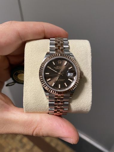 A person is holding a rolex watch in their hand.