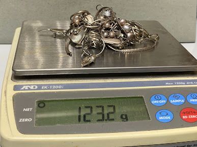 A pile of silver jewelry is being weighed on a scale.