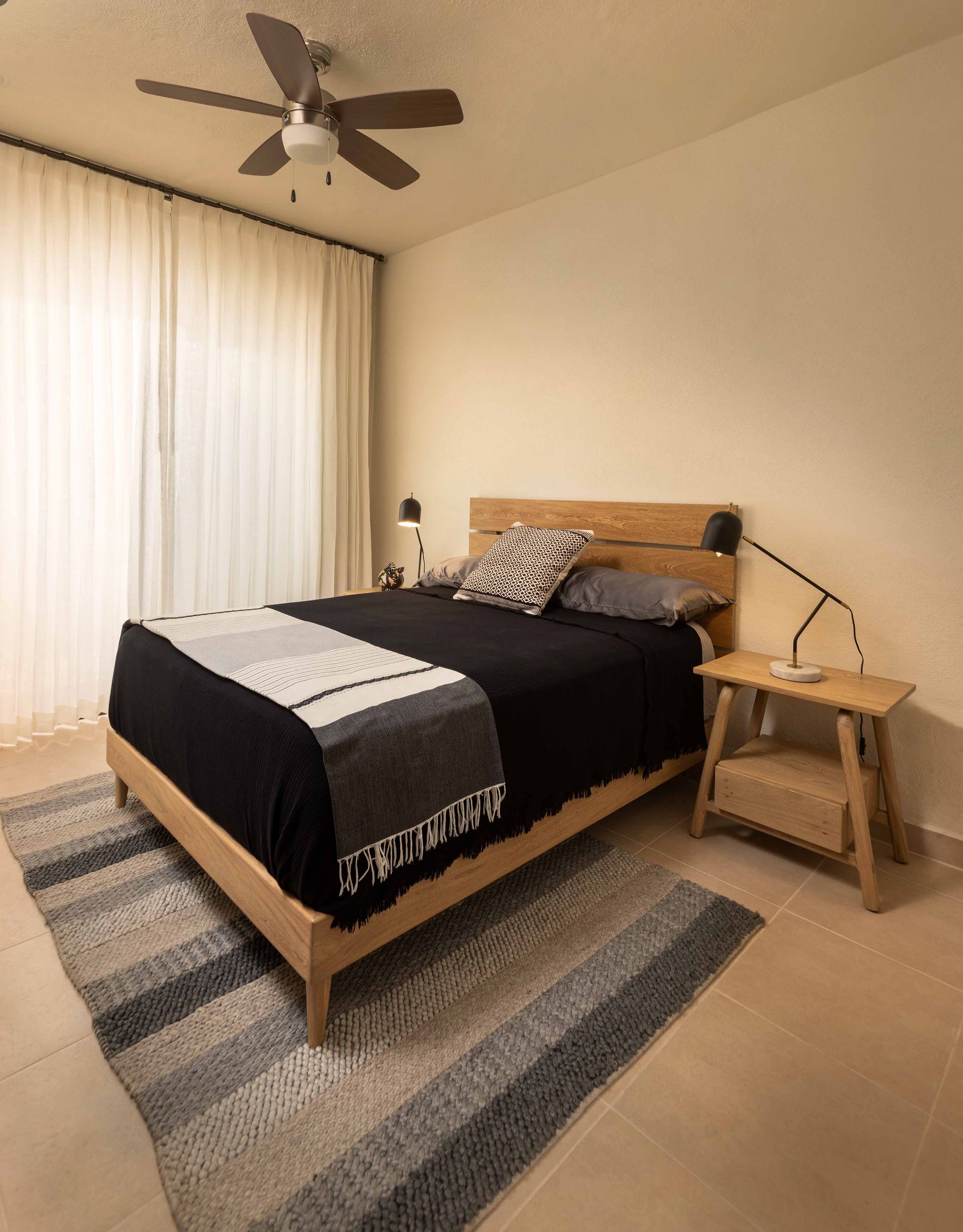 A bedroom with a bed , nightstand , rug and ceiling fan.