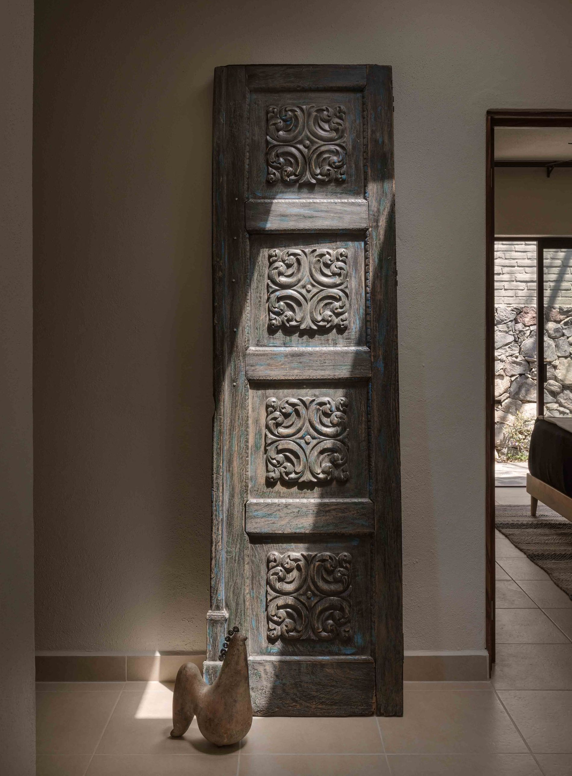 A statue of a chicken is sitting next to a carved wooden door in a hallway.