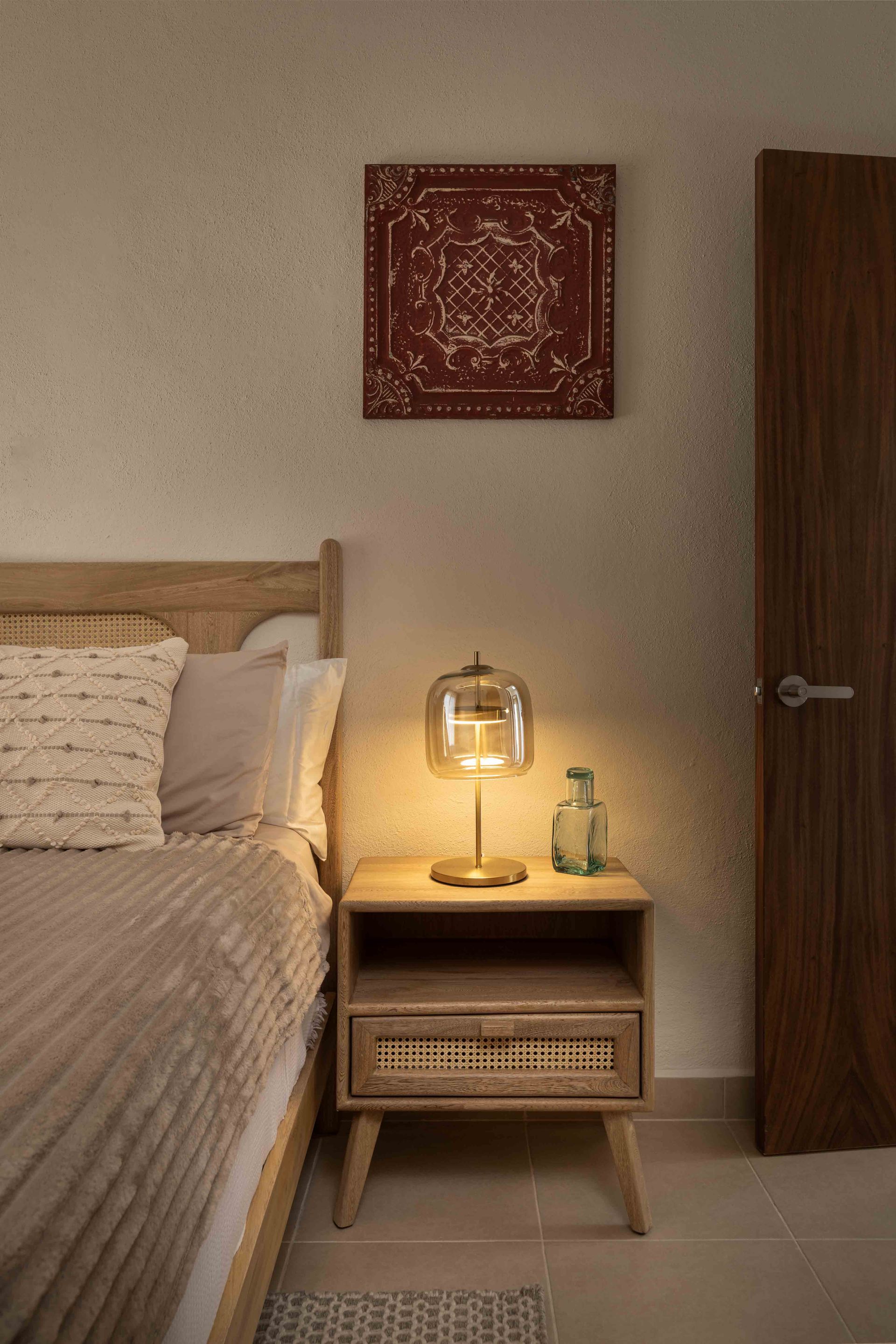 A bedroom with a bed , nightstand , lamp and painting on the wall.