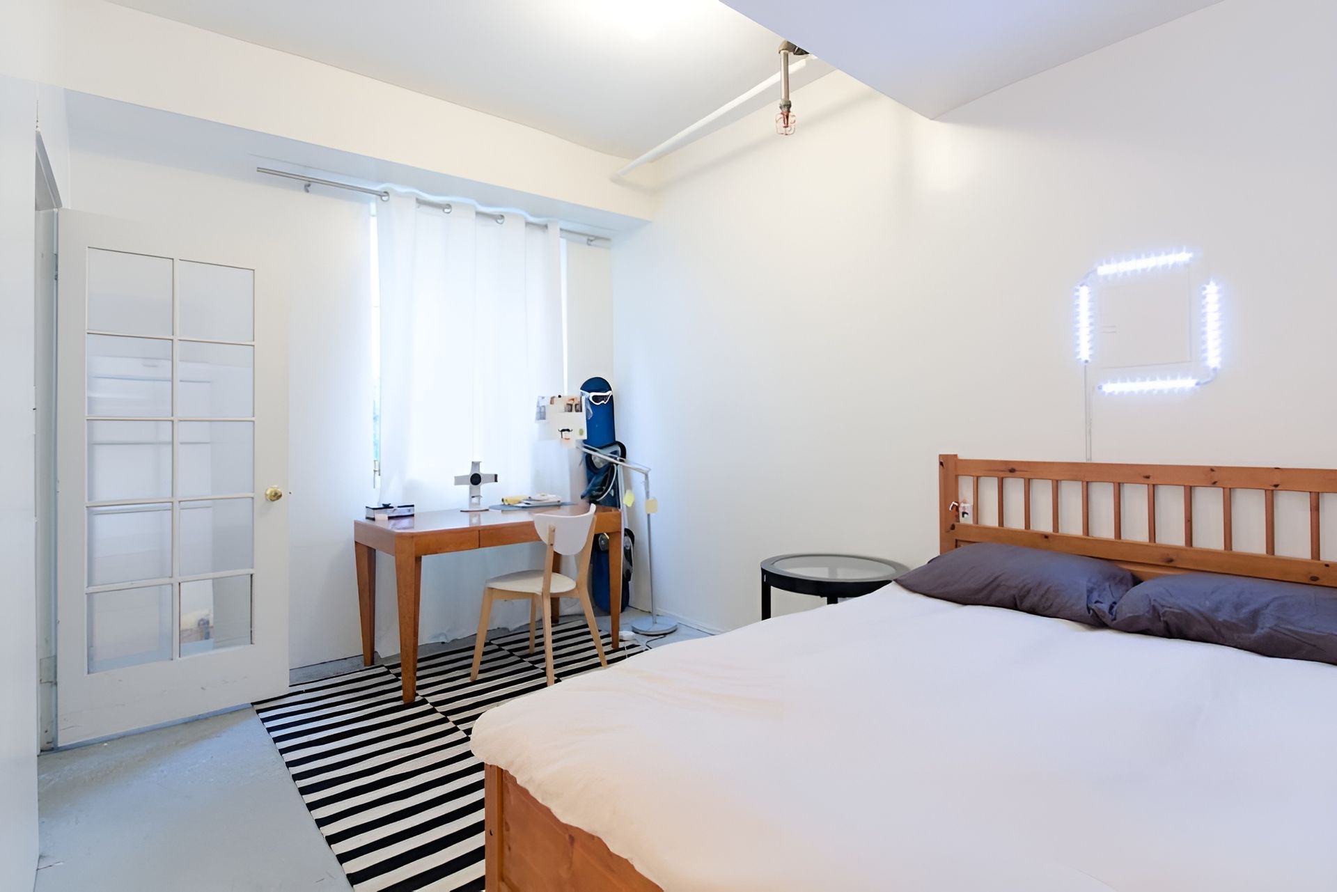 A bedroom with a bed a desk and a striped rug