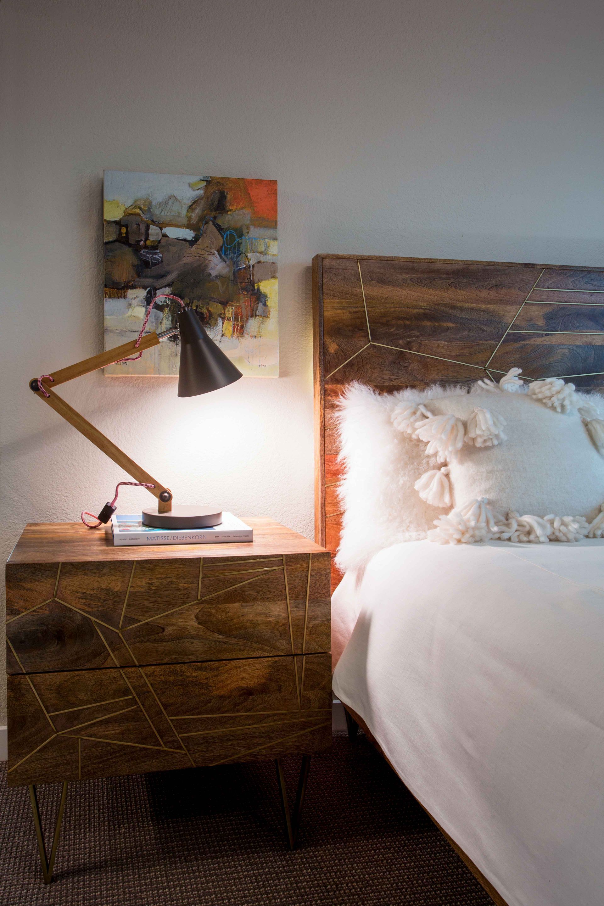 A bedroom with a bed , nightstand , lamp and painting on the wall.
