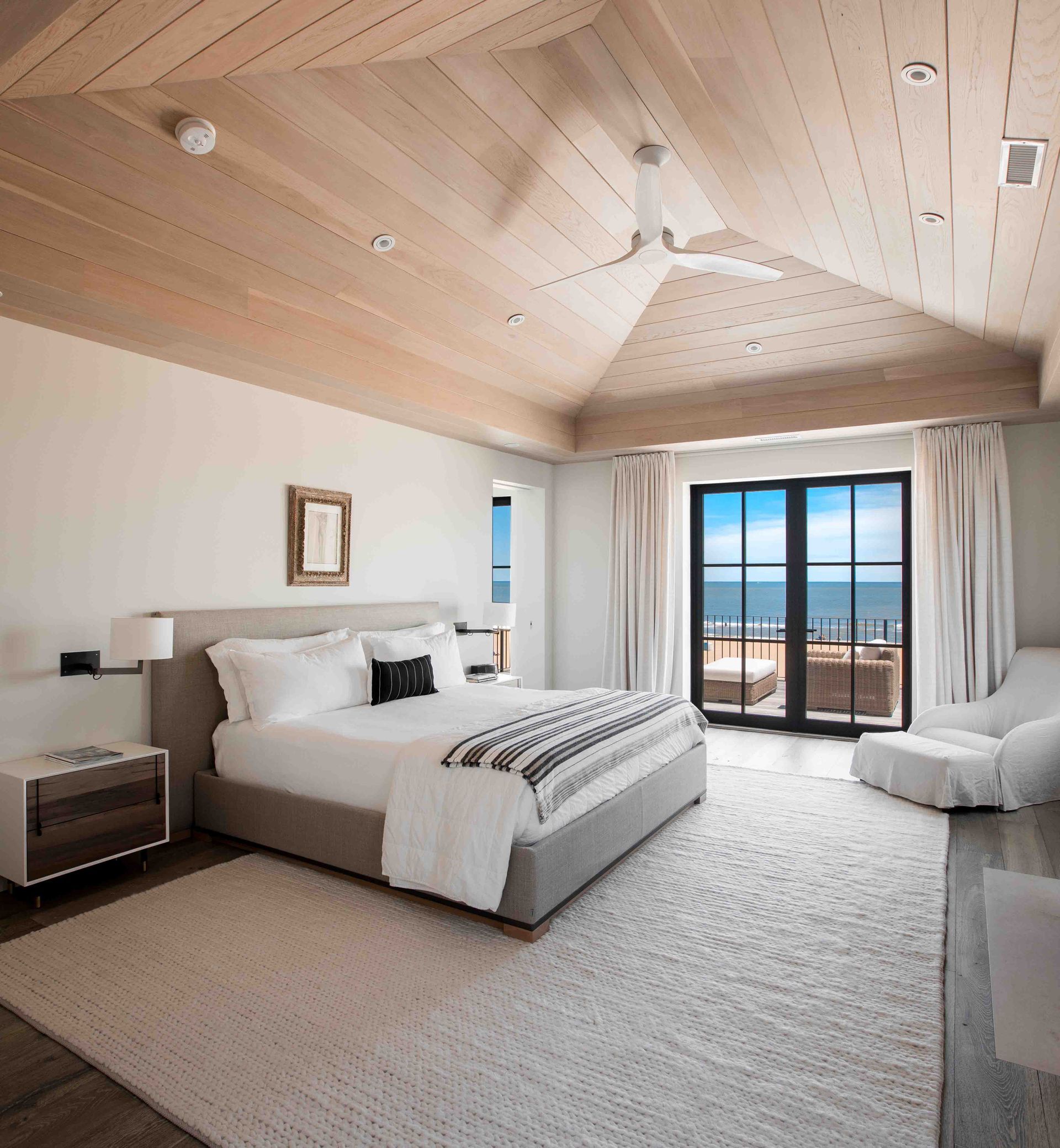A bedroom with a large bed and a large window overlooking the ocean.