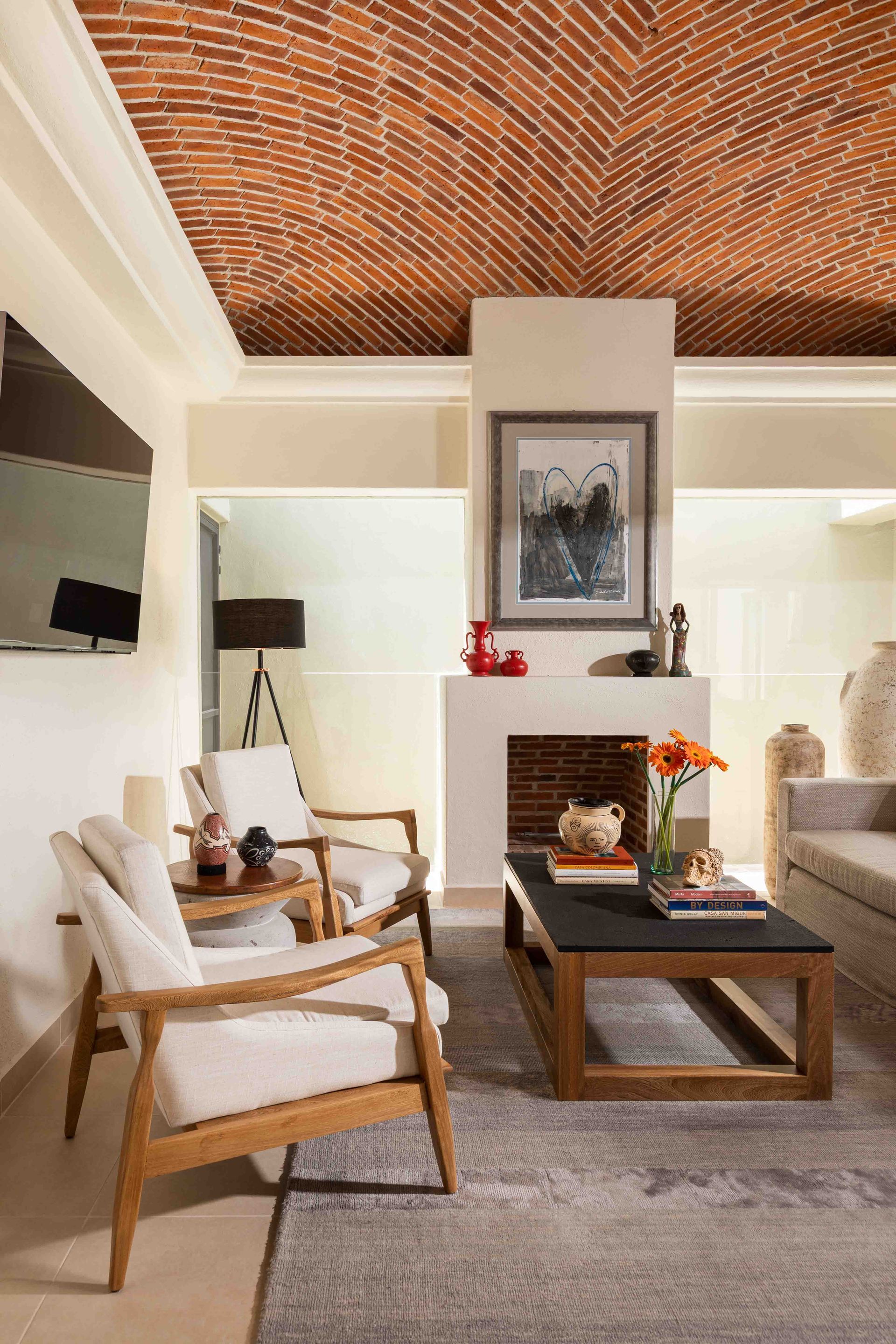 A living room with a brick ceiling , chairs , a coffee table and a fireplace.