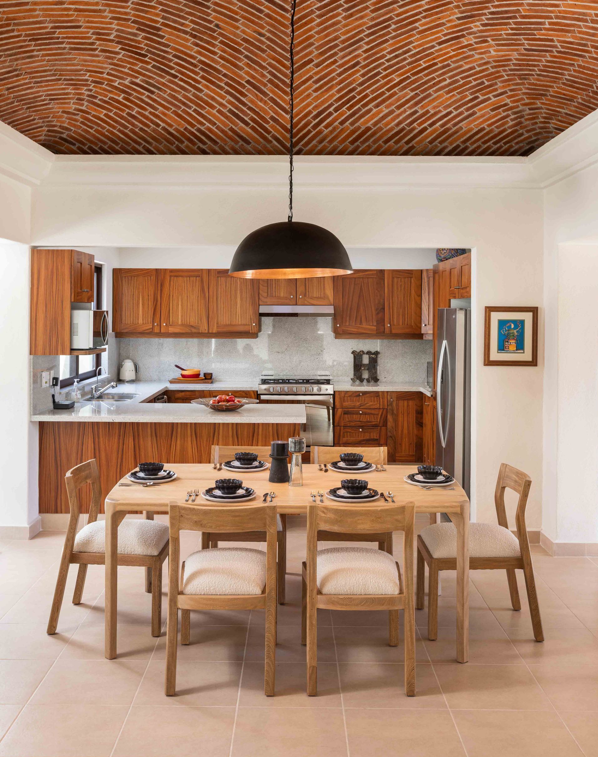 A dining room table and chairs in a kitchen with a brick ceiling.