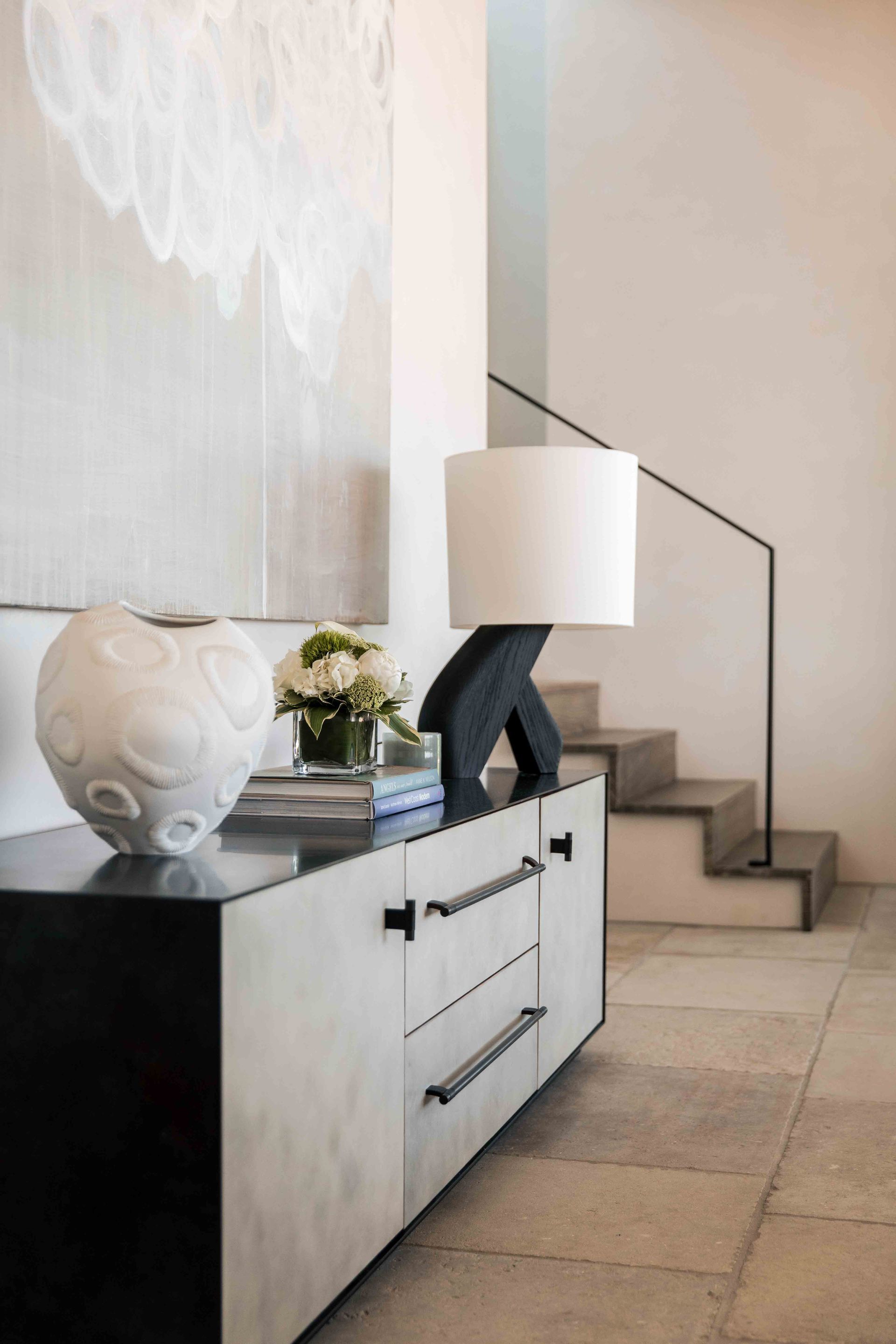 A dresser with a vase and a lamp on it next to a staircase.