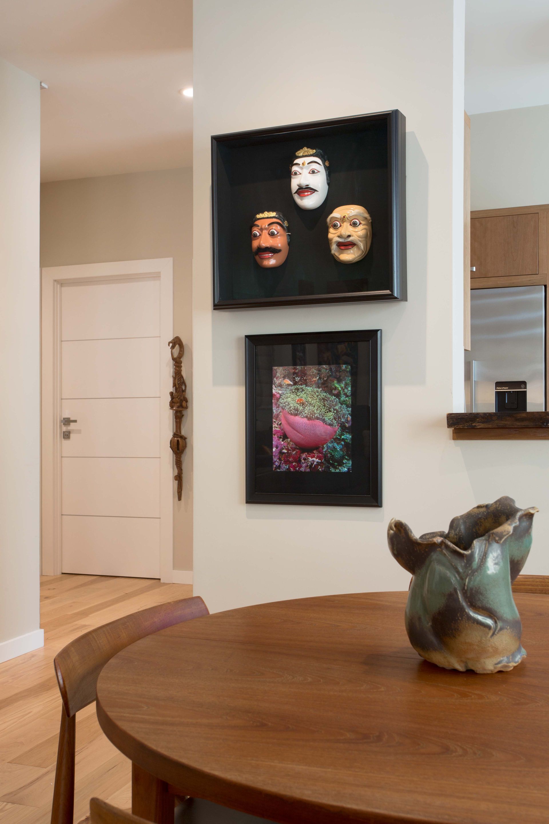 A dining room table with a vase on it and three framed masks on the wall above it