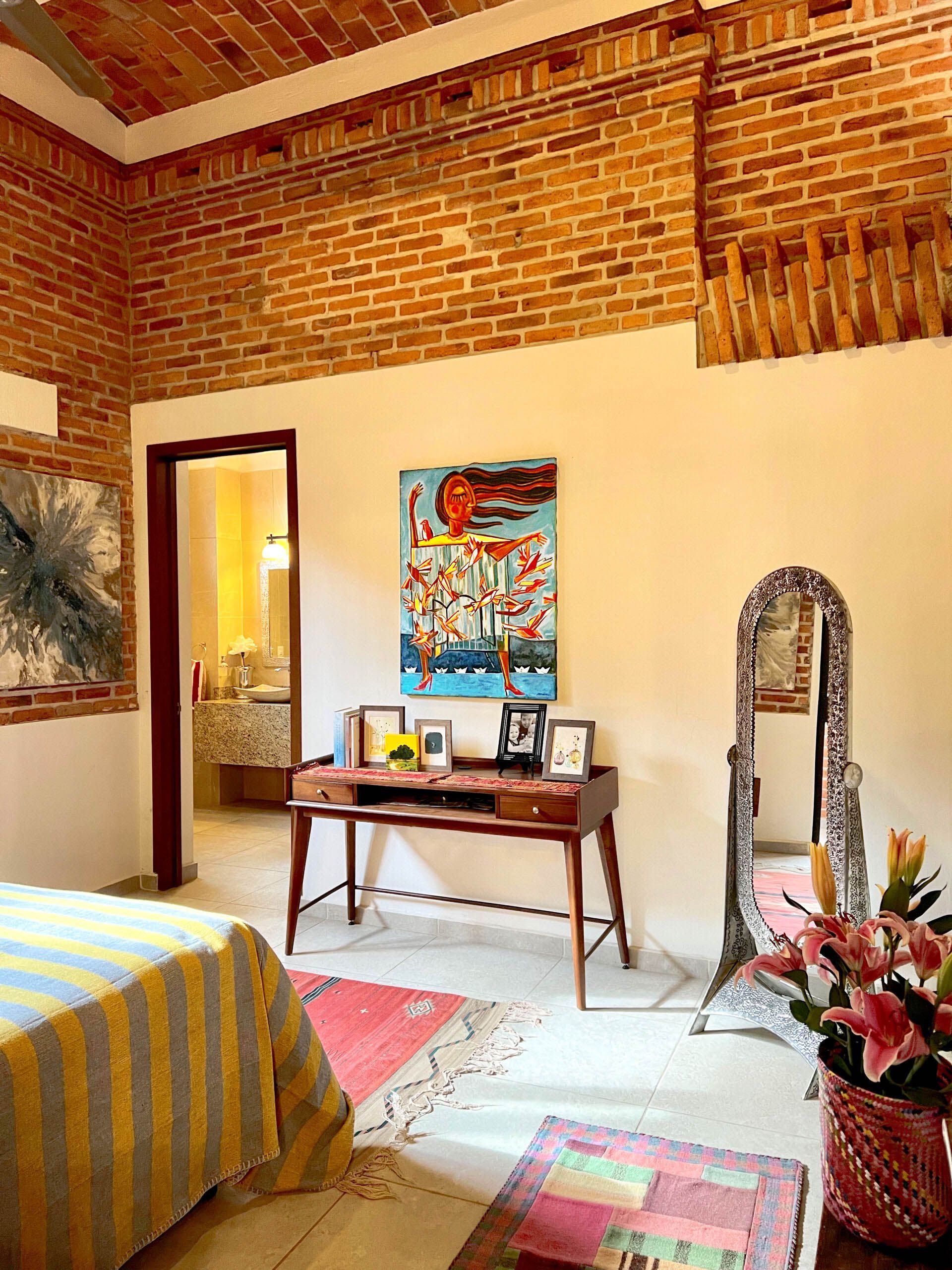 A bedroom with a bed , desk , mirror and painting on the wall.