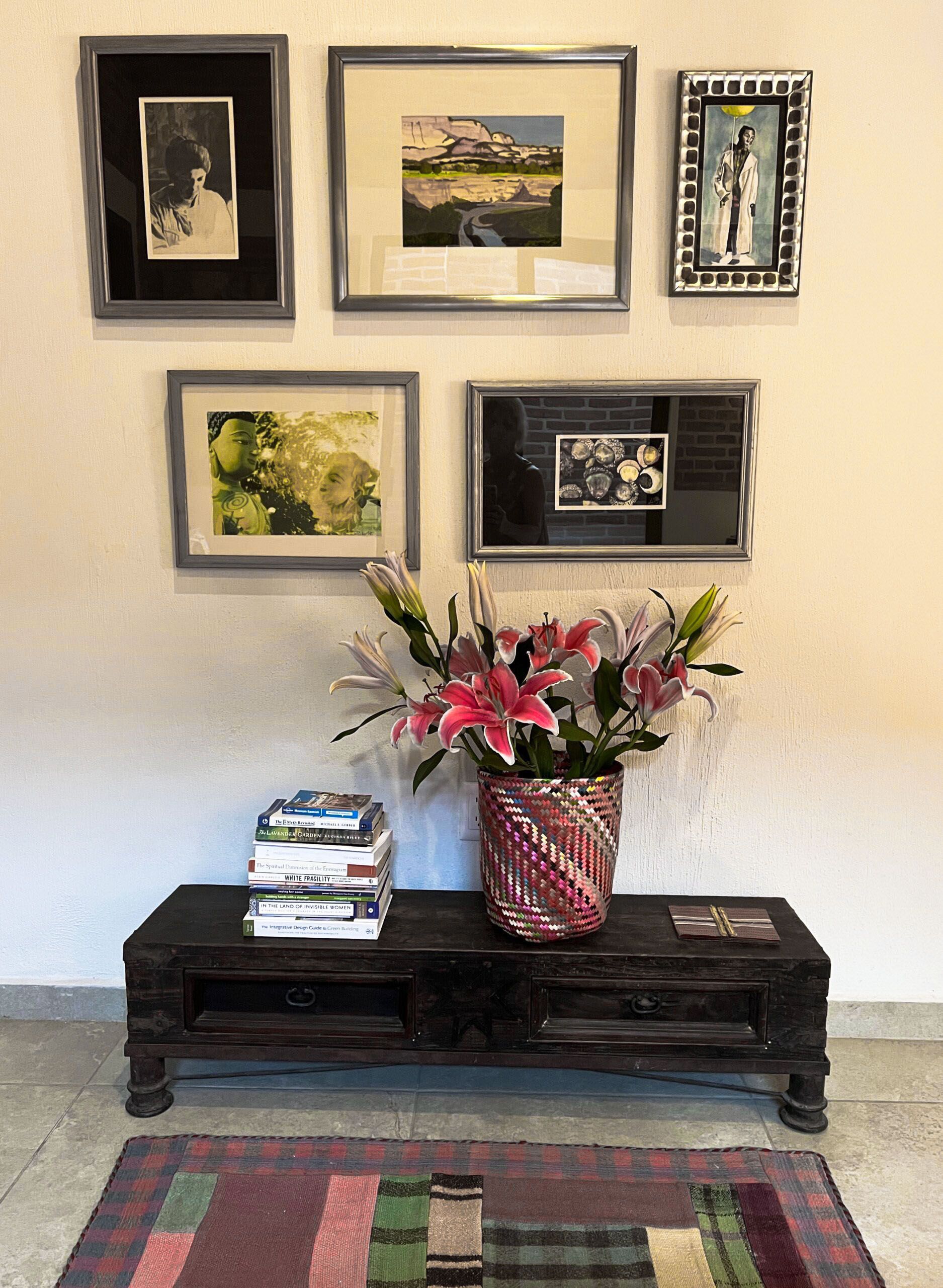 A vase of flowers is sitting on a table in front of a wall with pictures on it.