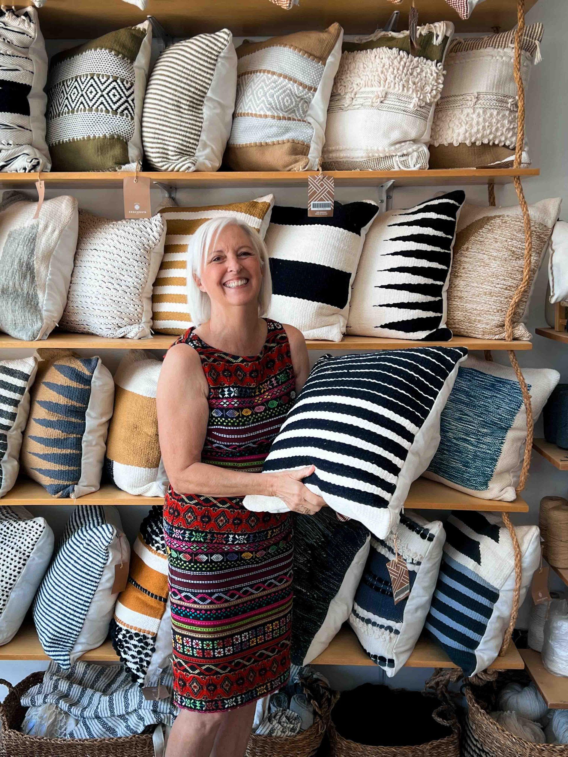A woman is holding a pillow in front of a shelf filled with pillows.