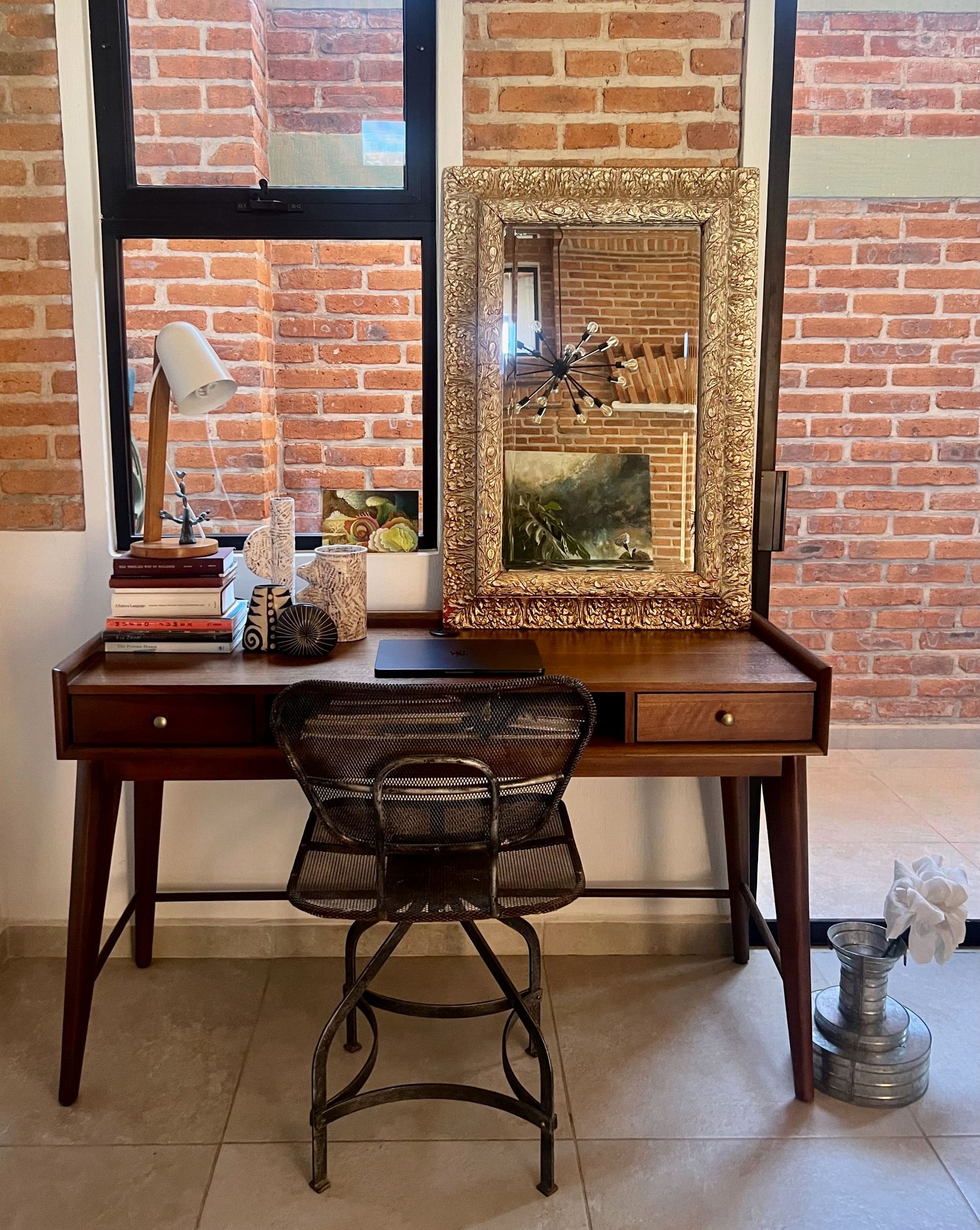 A desk with a chair and a mirror in front of a brick wall.