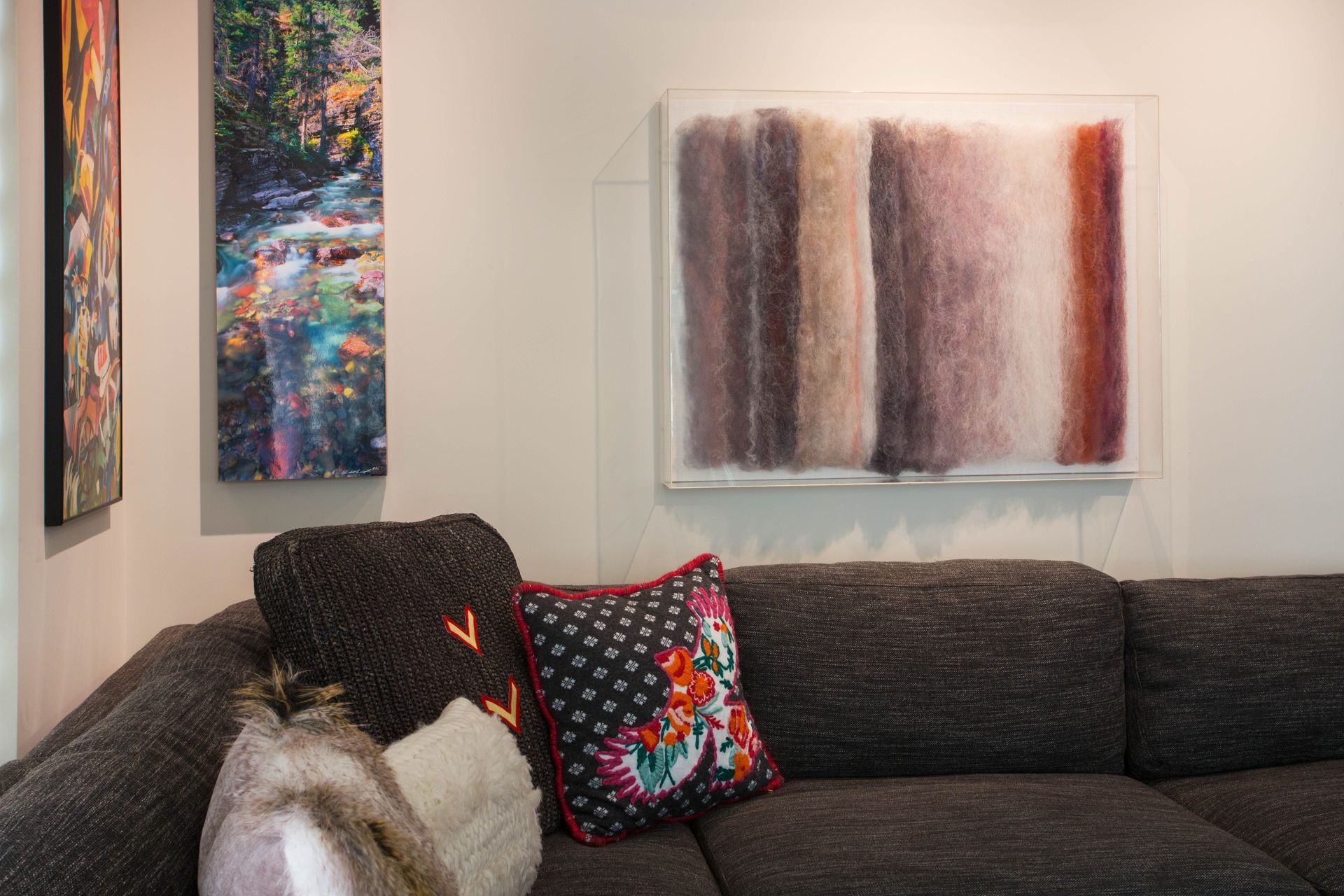 A living room with a couch , pillows and paintings on the wall.