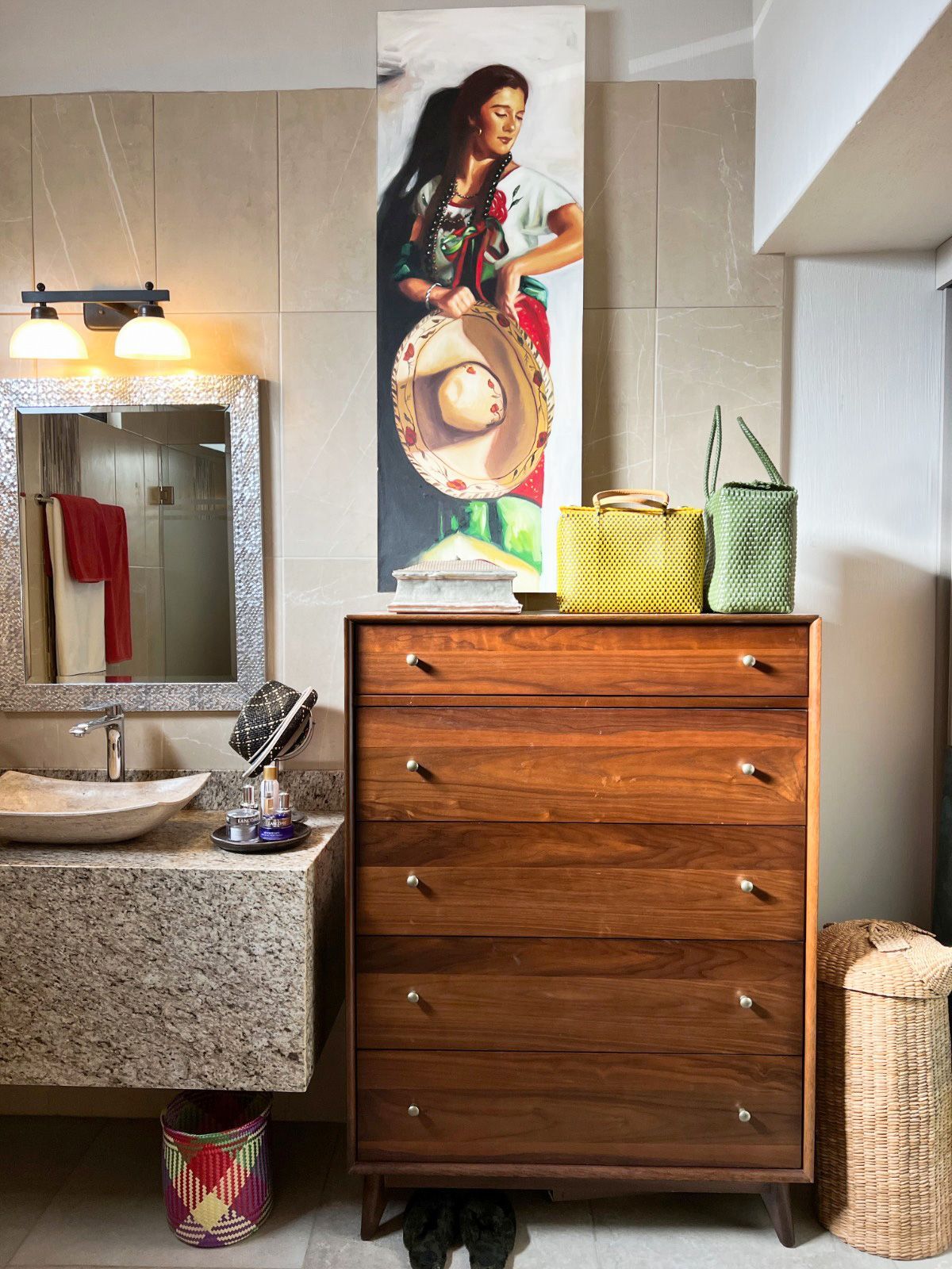 A bathroom with a dresser , sink , mirror and painting on the wall.