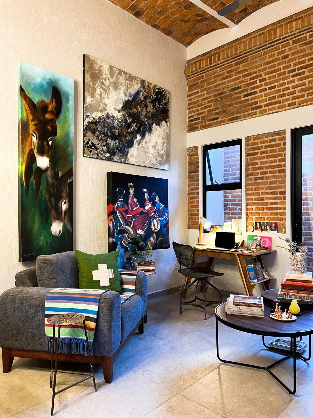A living room with a couch , chair , coffee table and paintings on the wall.