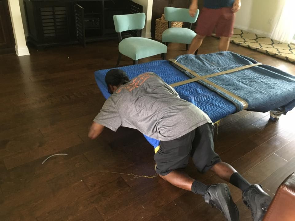 A man is laying on the floor next to a table covered in a blue blanket.