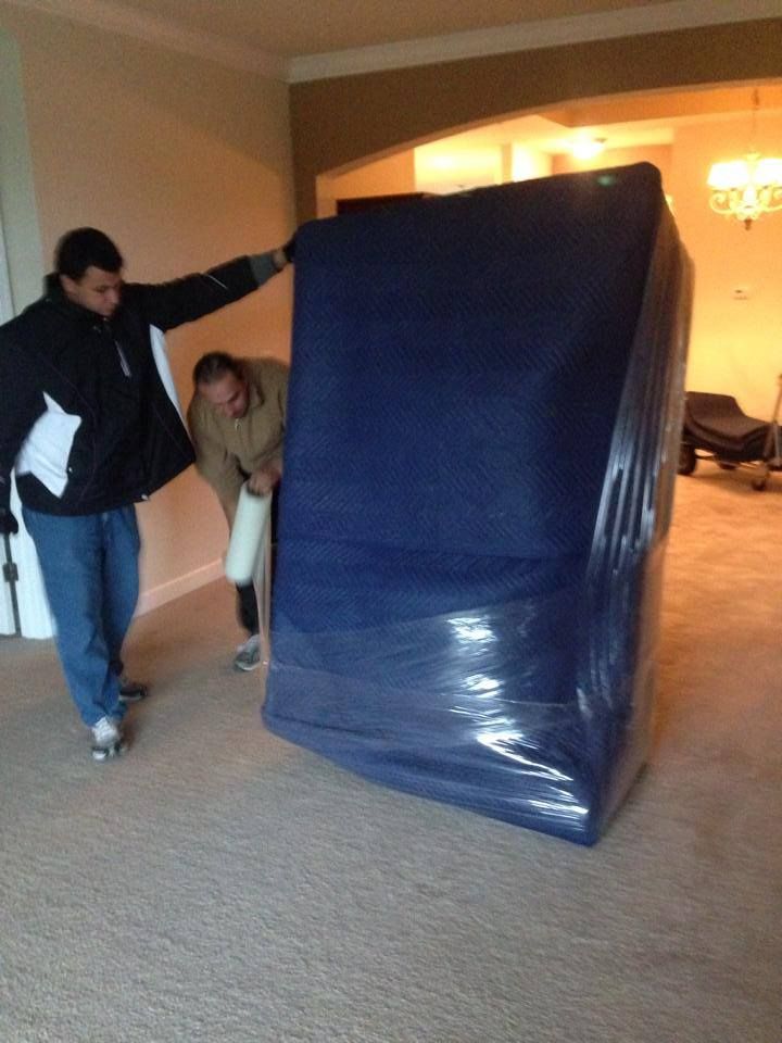 Two men carrying a large blue item wrapped in plastic