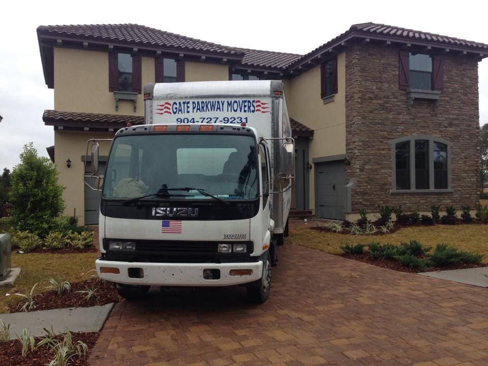 A white isuzu moving truck is parked in front of a large house