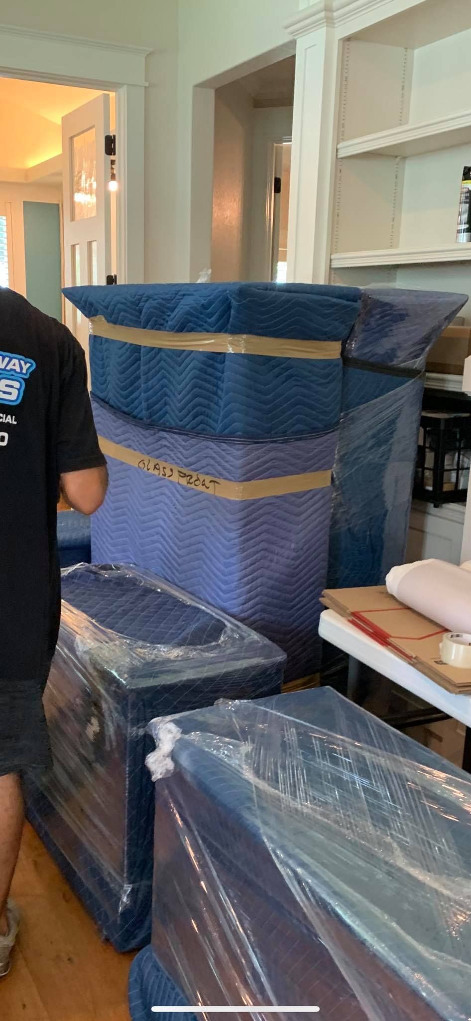 A man is standing next to a stack of boxes wrapped in plastic.
