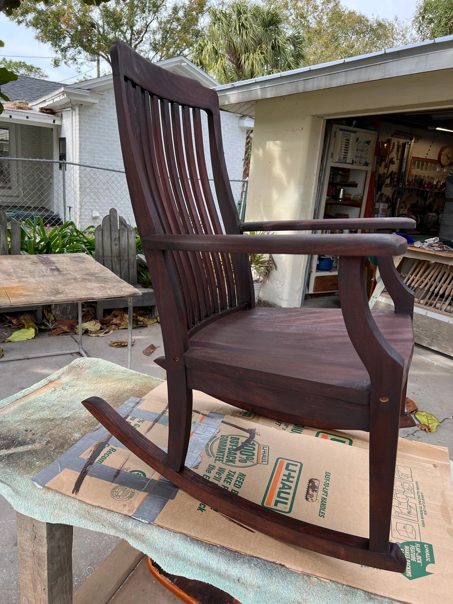 Dark wooden rocking chair outside, on a sheet covering a table.