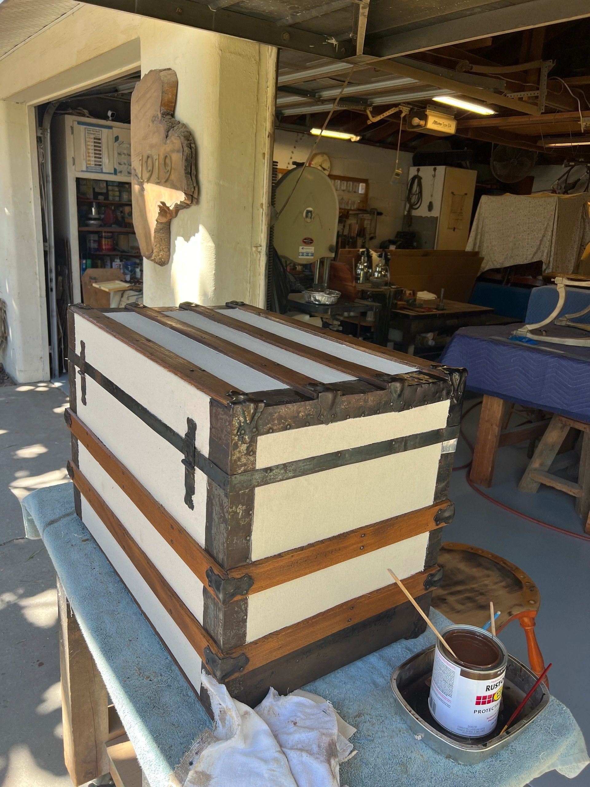 Antique trunk with white and brown stripes, metal accents, sitting on a work surface in a workshop.