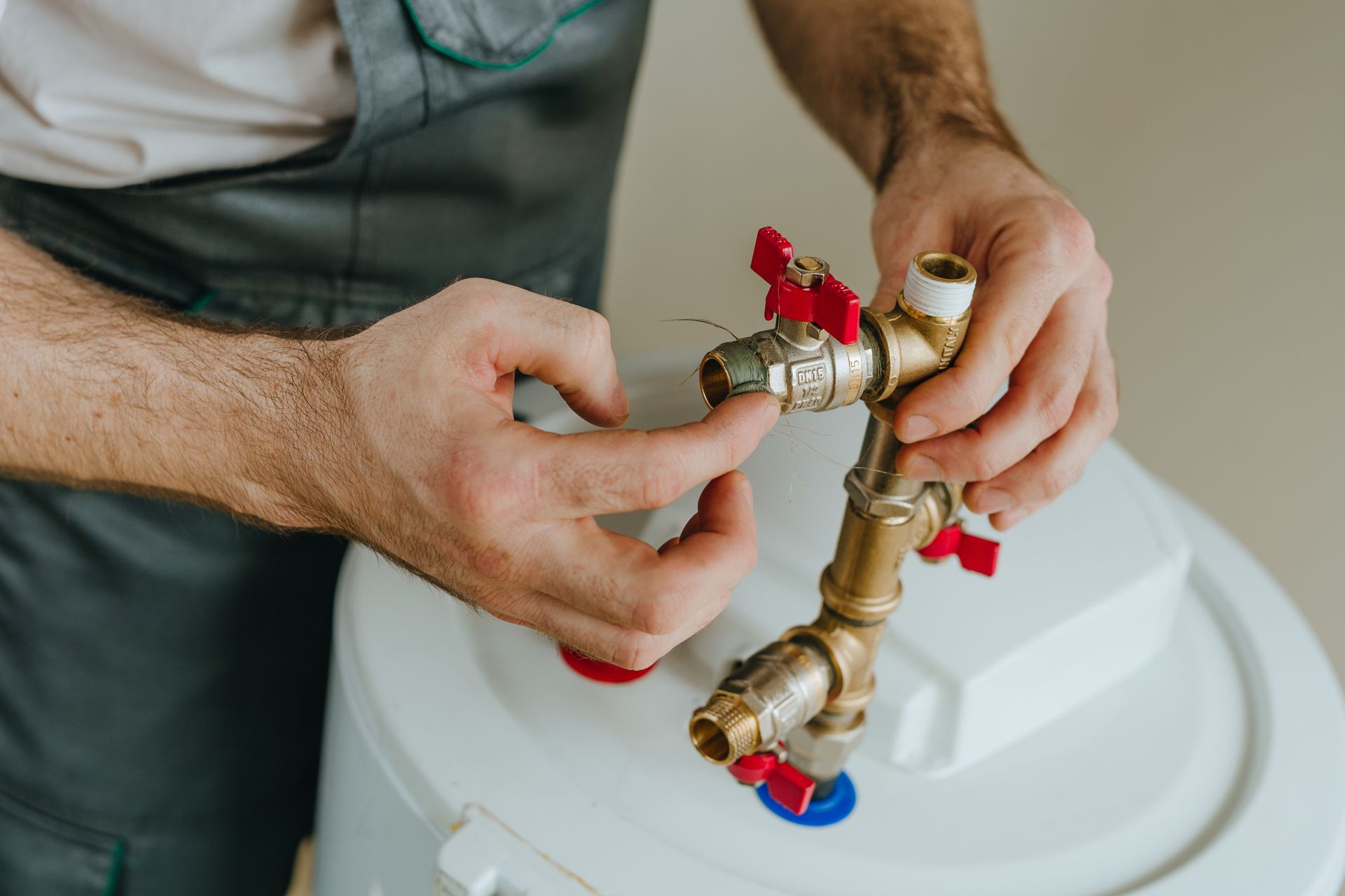 Close-up of a worker’s hands as he applies paste to the metal fitting of a water heater.