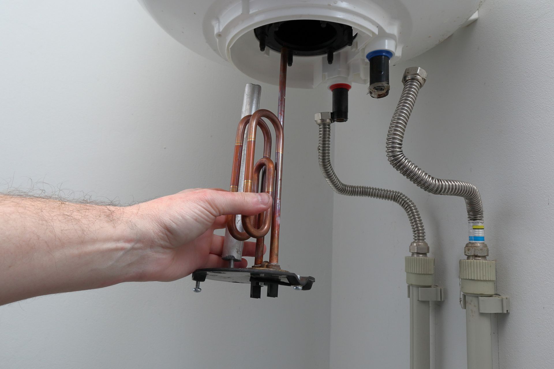 Hand removing water heater element for repair, showing hoses and wall-mounted unit maintenance.