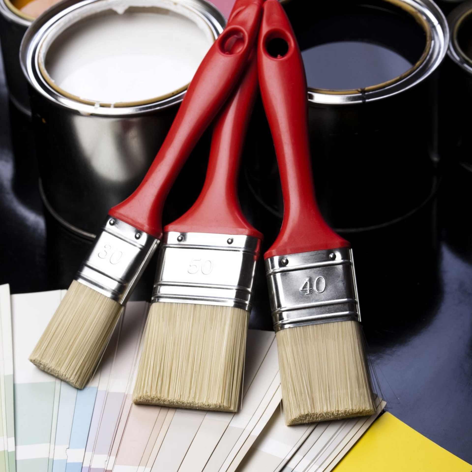 Pinceles apoyados sobre muestras de color, con latas de pintura en el fondo.